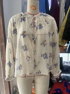 Detail of loose chiffon blouse with blue floral print, tie-neck and button closure