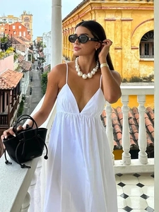 Detail of white V-neck backless maxi dress with large pearl necklace and black handbag