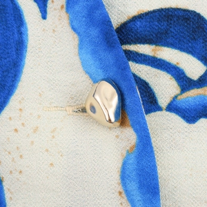 Detailed close-up of a fluid gold metal button on a blue abstract print dress fabric