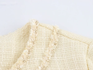 Vue détaillée du tissu en tweed crème avec des fils dorés et des détails de franges