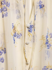 Close-up detail of V-neckline with fabric-covered buttons on floral pleated blouse