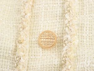 Vue détaillée du tweed crème avec bouton doré et bordure en chaîne métallique