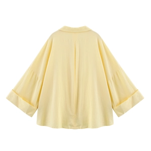 Back view of a loose pale yellow shirt featuring oversized cuffs and a center pleat detail