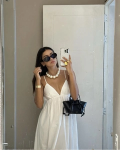 Detail of white deep V-neck backless maxi dress with pearl necklace and black knotted bag