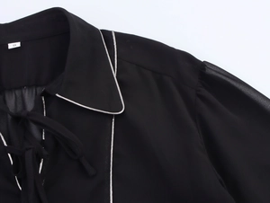 Detail of black chiffon shirt featuring white contrast piping and neckline tie design