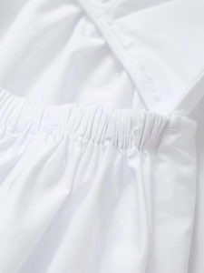 Detailed view of white dress featuring an elastic waist and criss-cross strap design