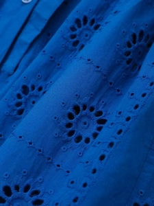 Detailed close-up of dark blue dress with intricate openwork floral embroidery and buttons