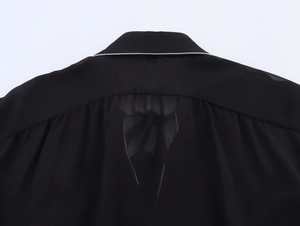 Detail view of black chiffon shirt back with white piping trim and pleated design