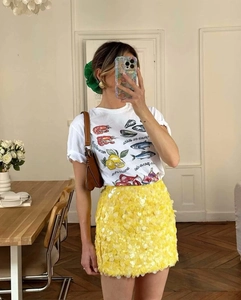 Detail of a bright yellow sequin mini skirt paired with a white graphic t-shirt for summer