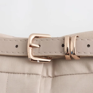 Detail of a thin beige belt with a polished rose gold square buckle and neat stitching