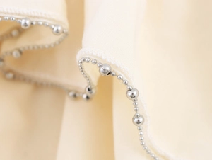 Macro view of cream fabric ruffled edge with silver metal bead chain detailing