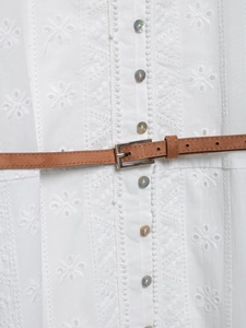 Gros plan détaillé de broderie florale blanche avec boutons en nacre et fine ceinture en cuir