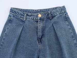 Détail de jean taille haute avec plis, bouton doré et tissu denim bleu foncé délavé