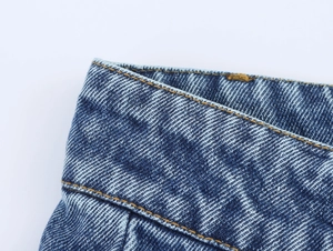 Gros plan sur un tissu denim bleu foncé avec coutures contrastées et texture délavée