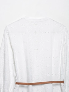 Détail de la robe blanche en broderie anglaise avec manches longues et fine ceinture en cuir
