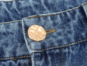 Détail d'un bouton doré vintage sur un jean bleu foncé avec des coutures contrastées