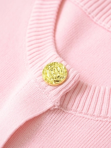 Detailed close-up of pink ribbed knit texture and gold button with rose engraving