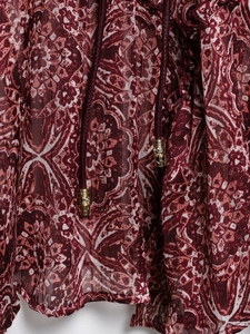 Détail d'une robe en mousseline paisley rouge avec fils métalliques et embouts dorés