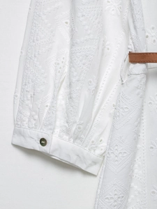 Détail d'une robe chemise blanche brodée avec des motifs ajourés et une ceinture marron