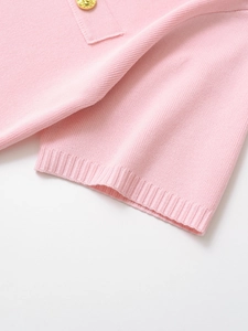 Detail of pink knit short sleeve dress with gold floral button and ribbed cuff texture