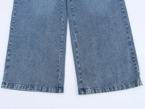 Détail de l'ourlet large sur un jean en denim bleu délavé avec coutures nettes et texture