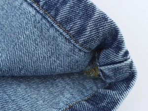 Vue détaillée du tissu denim bleu indigo avec des coutures renforcées en fil doré