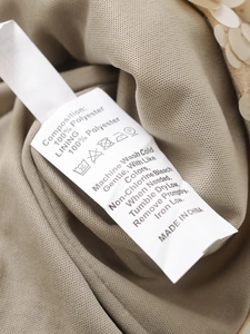 Detailed macro view of khaki knit fabric with yellow sequins and 100% polyester wash label