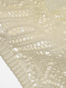 Close-up of cream lace crochet fabric showing intricate hollow knit patterns and texture