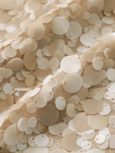 Detail shot of multi-sized matte beige sequins sewn onto delicate chiffon fabric