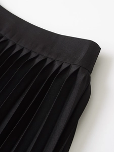 Close-up of high-waisted black pleated skirt showing accordion folds and twill texture