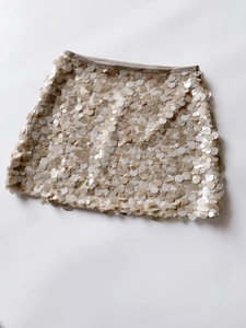 Detailed view of beige sequin mini skirt with shimmering circular discs and fabric edge