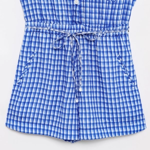 Detail of blue gingham romper showing button closure, drawstring waist and side pockets