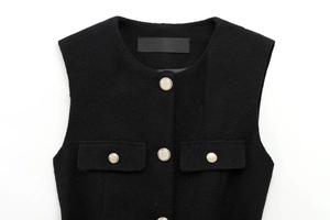 Detail of black tweed vest featuring textured fabric and decorative gold metal buttons