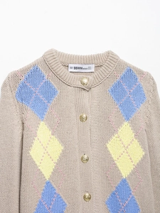 Detailed macro view of beige knit cardigan featuring embossed gold buttons and brand neck label