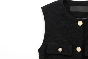 Detailed macro of black tweed vest fabric featuring ornate gold textured buttons