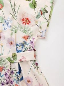 Detail of floral print summer dress featuring gold metal buttons and a matching waist belt