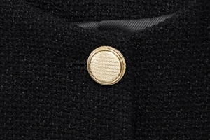 Detail of round golden embossed metal button on black tweed vest with rich texture