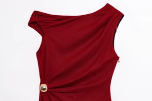 Detail of burgundy sleeveless dress featuring asymmetric drape and gold ball hardware
