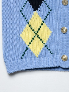 Detailed close-up of blue argyle knit sweater with embossed gold metal buttons