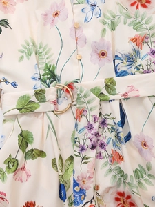 Detail of silk-textured dress featuring floral print, gold buttons, and belted waist buckle
