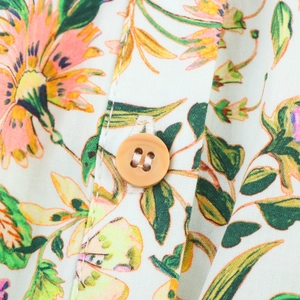 Detail view of pink floral print on white cotton fabric with a round brown button