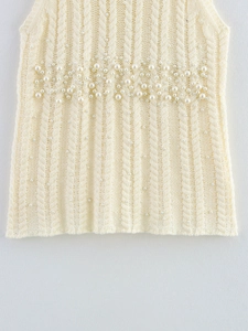 Detail of cable knit texture with pearl embellishments on a cream knit top