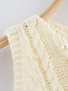 Macro detail of white cable knit short sleeve sweater with elegant pearl embellishments