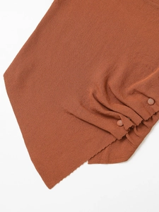 Close-up of burnt orange knitted shirt showing ribbed texture and buttoned pleated hem