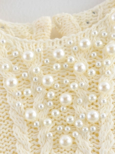 Detail of cream cable knit top featuring elegant faux pearl embellishments on the neckline