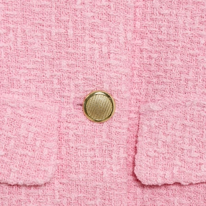 Close-up of pink tweed fabric texture and a gold embossed button on the stylish vest