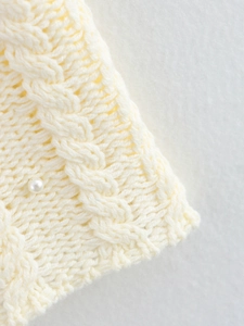 Close-up of ivory cable-knit texture featuring an elegant faux pearl embellishment