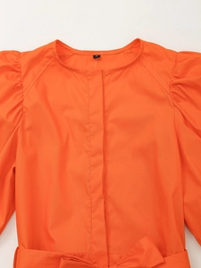 Détail de la robe orange avec manches bouffantes, plis et une ceinture à la taille