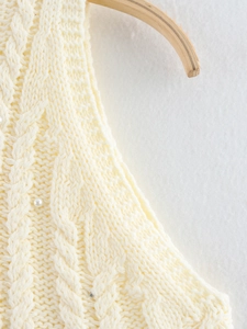 Detailed macro view of cable knit texture and faux pearl beads on a cream women's knit top