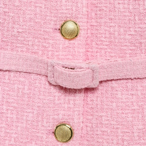 Close-up of pink tweed fabric texture with gold metallic buttons and woven waist detail